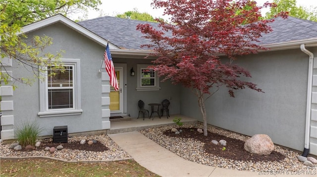 property entrance featuring a shingled roof and stucco siding