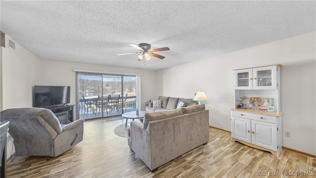 living area featuring baseboards, visible vents, light wood-style flooring, ceiling fan, and a textured ceiling