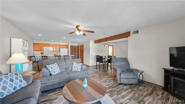 living area with baseboards, visible vents, ceiling fan, wood finished floors, and a textured ceiling