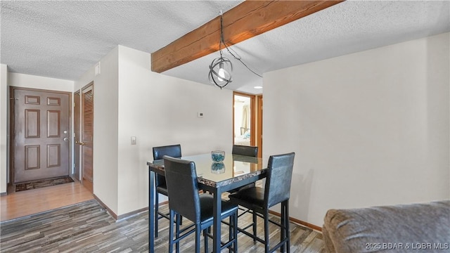 dining area with beamed ceiling, a textured ceiling, baseboards, and wood finished floors