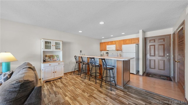 kitchen with white appliances, light wood-style floors, open floor plan, light countertops, and a kitchen bar