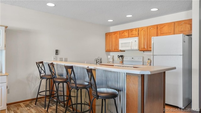 kitchen with a textured ceiling, white appliances, a kitchen breakfast bar, light countertops, and light wood-type flooring