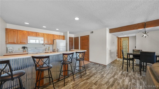 kitchen featuring white appliances, light countertops, a breakfast bar area, and wood finished floors