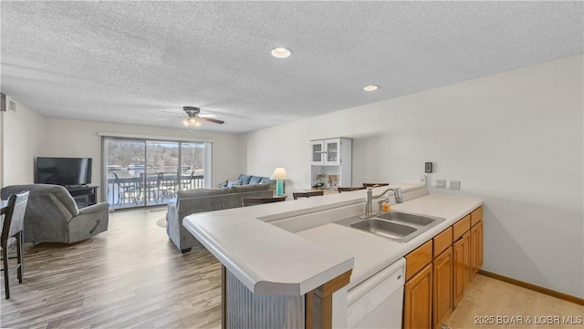 kitchen with brown cabinets, open floor plan, white dishwasher, light wood-type flooring, and a sink