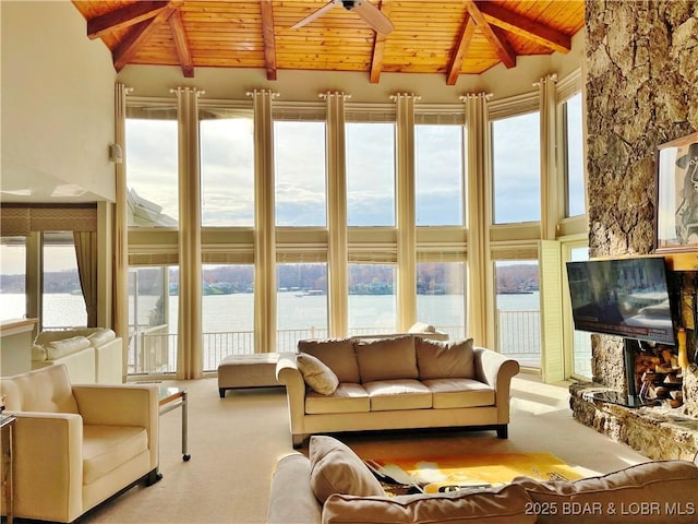 sunroom with vaulted ceiling with beams, wooden ceiling, a ceiling fan, and a stone fireplace