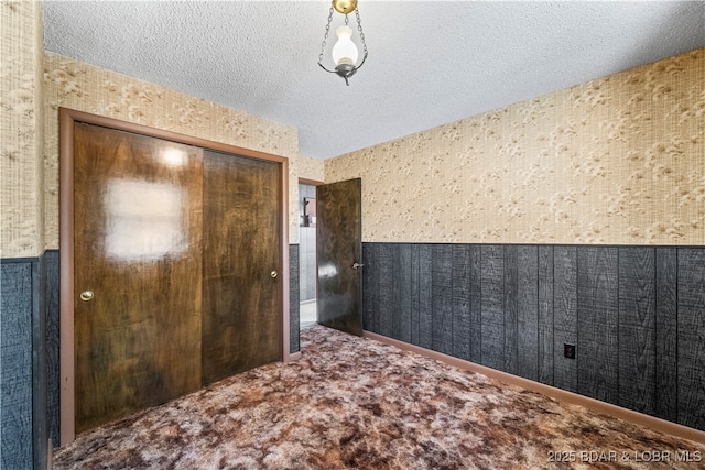 interior space featuring a closet, a wainscoted wall, a textured ceiling, and wallpapered walls