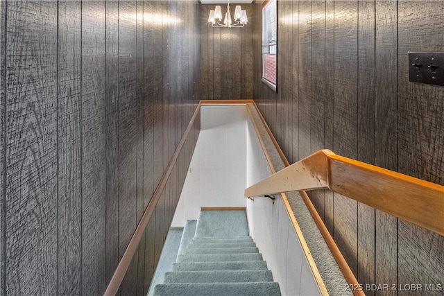 staircase with wood walls and an inviting chandelier