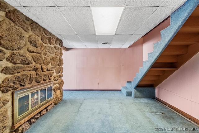 finished below grade area featuring carpet, a fireplace, a drop ceiling, baseboards, and stairs