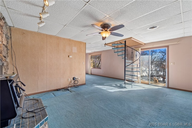 unfurnished living room with stairway, carpet flooring, visible vents, and wooden walls