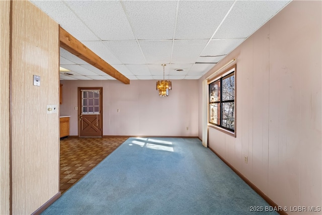 empty room featuring baseboards, carpet flooring, a paneled ceiling, wood walls, and a notable chandelier