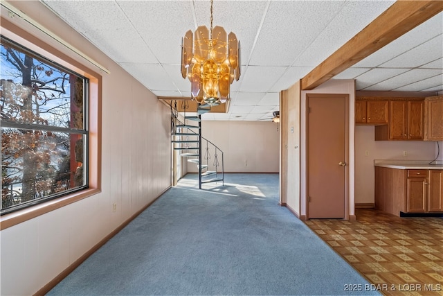 interior space featuring carpet, baseboards, stairway, and a drop ceiling