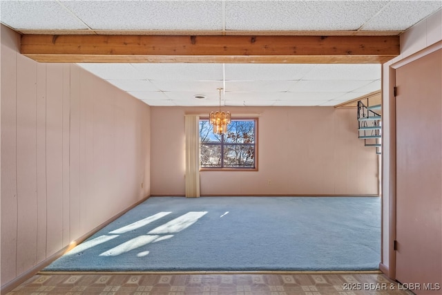 carpeted spare room with a chandelier, a paneled ceiling, wooden walls, and baseboards