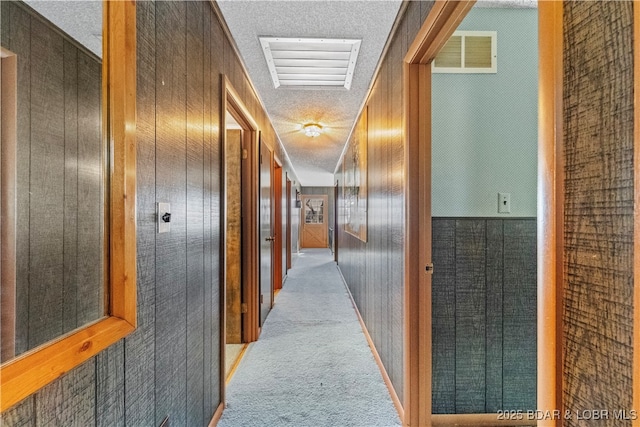 hallway featuring carpet, visible vents, wood walls, and a textured ceiling