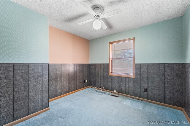 carpeted empty room with a ceiling fan, a textured ceiling, and wainscoting