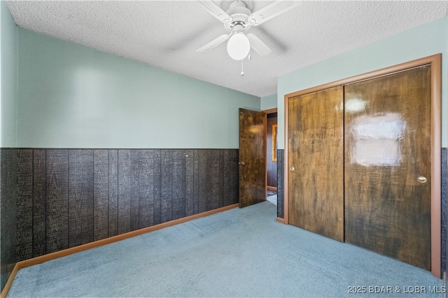 unfurnished bedroom featuring wainscoting, ceiling fan, carpet, a textured ceiling, and a closet