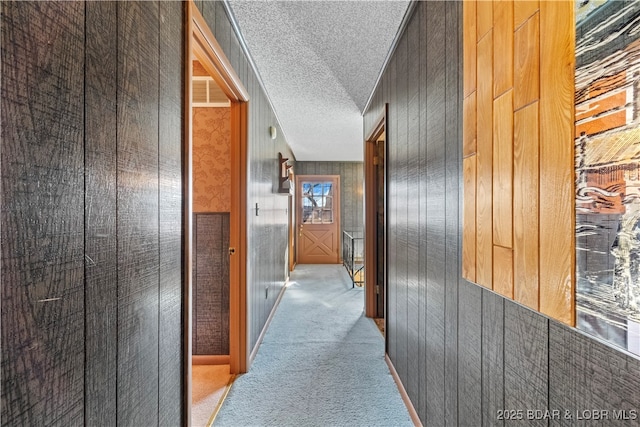 corridor featuring wooden walls, visible vents, carpet flooring, and a textured ceiling