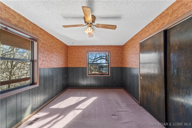 spare room with wallpapered walls, visible vents, a wainscoted wall, a textured ceiling, and carpet flooring