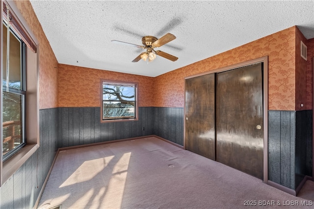 unfurnished bedroom with wallpapered walls, visible vents, wainscoting, a textured ceiling, and a closet