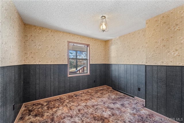 empty room featuring a textured ceiling, carpet floors, and wainscoting