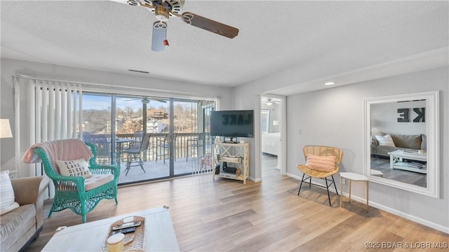 living area featuring a ceiling fan, a textured ceiling, baseboards, and wood finished floors