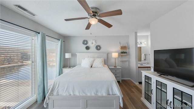 bedroom with connected bathroom, a textured ceiling, visible vents, and dark wood-style flooring