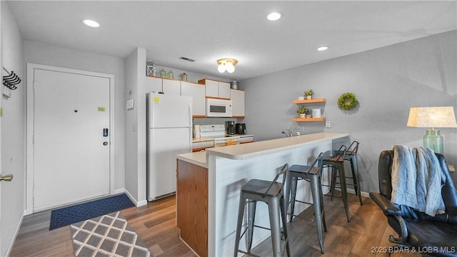 kitchen with light countertops, white appliances, wood finished floors, and a breakfast bar