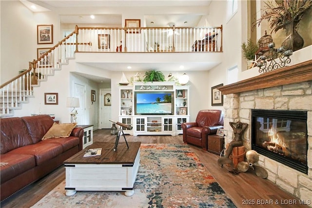 living area featuring a high ceiling, stairway, a fireplace, and wood finished floors