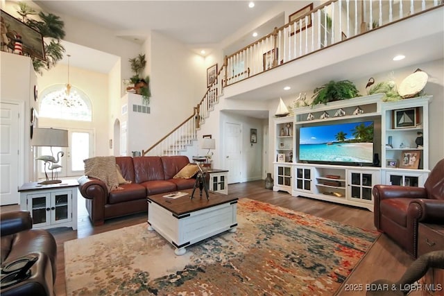 living area with arched walkways, a notable chandelier, wood finished floors, a towering ceiling, and stairway