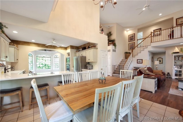 dining space with light tile patterned floors, recessed lighting, stairway, a high ceiling, and ceiling fan with notable chandelier