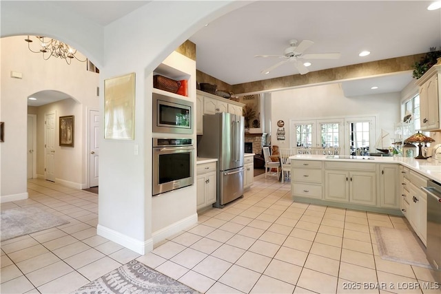 kitchen with light tile patterned floors, ceiling fan, arched walkways, stainless steel appliances, and a peninsula