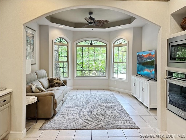 living area with a ceiling fan, a tray ceiling, light tile patterned flooring, and baseboards