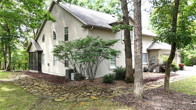 view of side of home with a sunroom, roof with shingles, central AC unit, and stucco siding