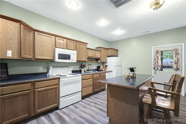 kitchen with dark countertops, white appliances, visible vents, and a breakfast bar area