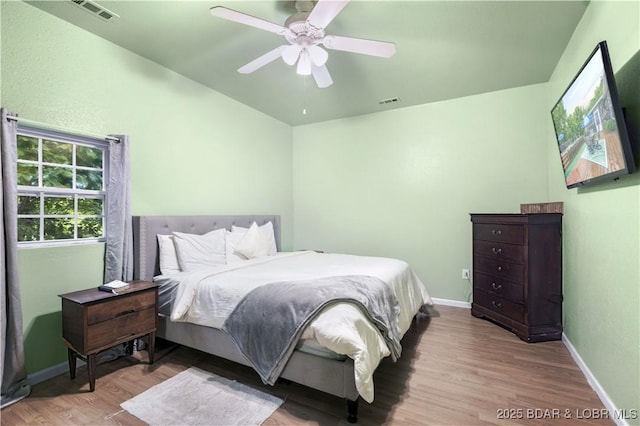 bedroom with ceiling fan, wood finished floors, visible vents, and baseboards