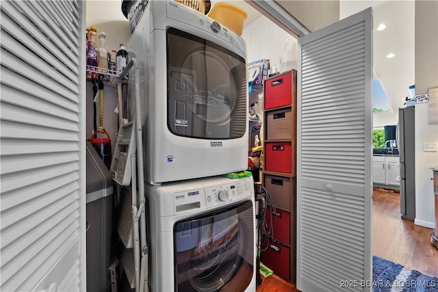 laundry room with recessed lighting, laundry area, stacked washer and dryer, a sink, and wood finished floors