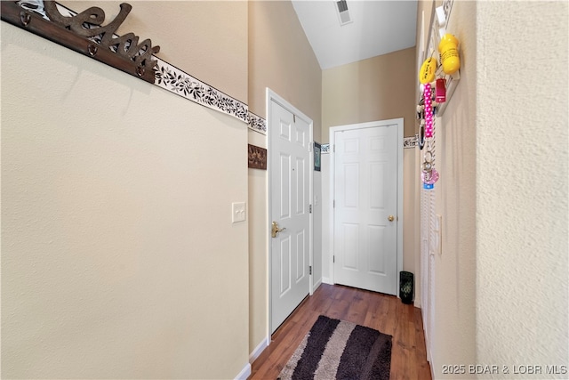 corridor featuring lofted ceiling, baseboards, visible vents, and wood finished floors