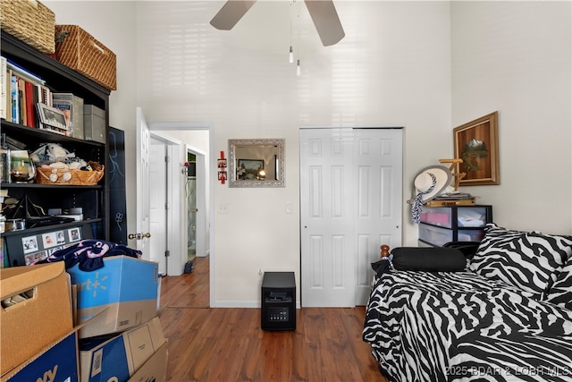 bedroom featuring a towering ceiling, a closet, a ceiling fan, and wood finished floors