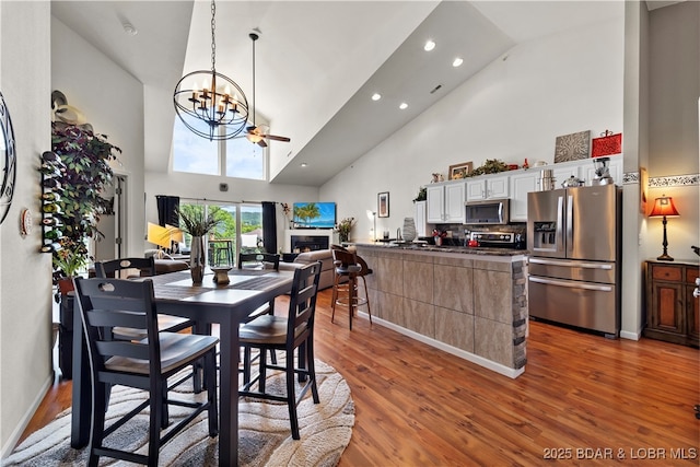 dining space with a notable chandelier, a fireplace, light wood-style flooring, high vaulted ceiling, and baseboards