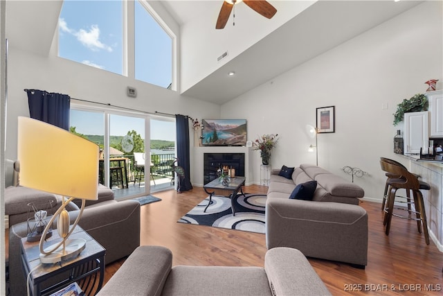 living room featuring baseboards, visible vents, a glass covered fireplace, ceiling fan, and wood finished floors