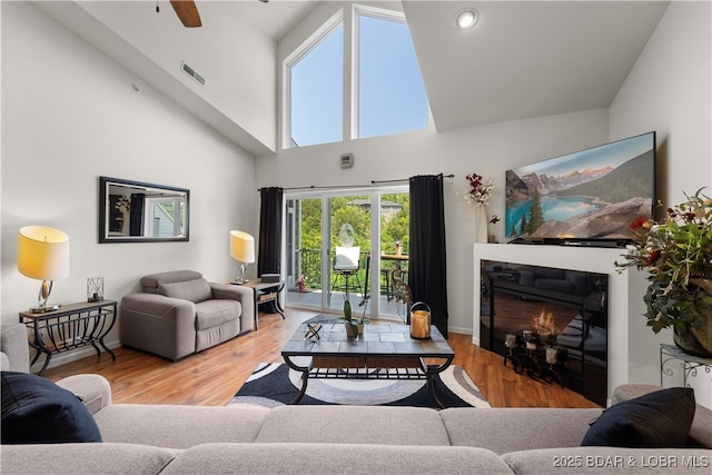 living area with high vaulted ceiling, visible vents, wood finished floors, and a glass covered fireplace