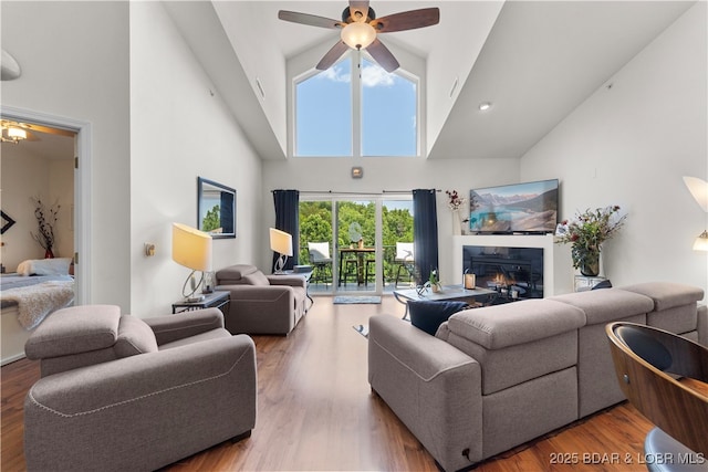 living area featuring ceiling fan, high vaulted ceiling, wood finished floors, and a glass covered fireplace