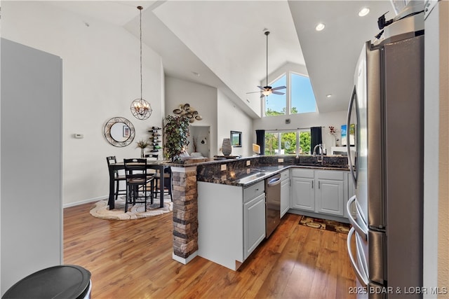 kitchen with stainless steel appliances, light wood-style floors, open floor plan, high vaulted ceiling, and a peninsula