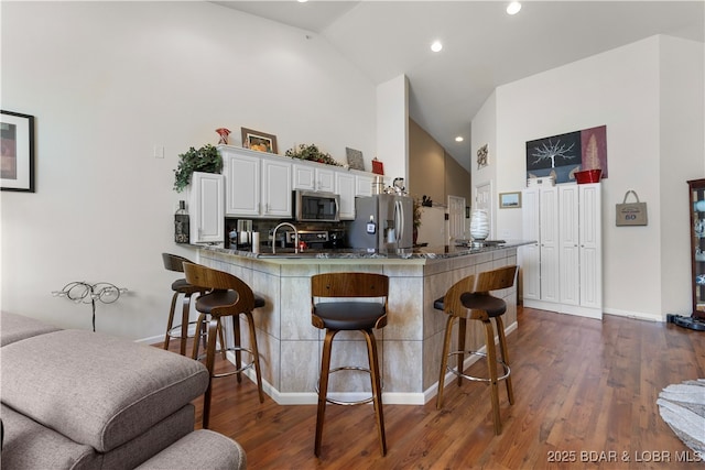 kitchen featuring stainless steel appliances, a breakfast bar area, a peninsula, and dark wood finished floors