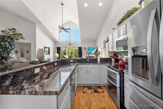 kitchen featuring stainless steel appliances, a sink, white cabinets, open floor plan, and light wood-style floors