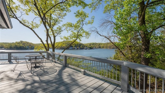 wooden deck with outdoor dining area, a water view, and a wooded view