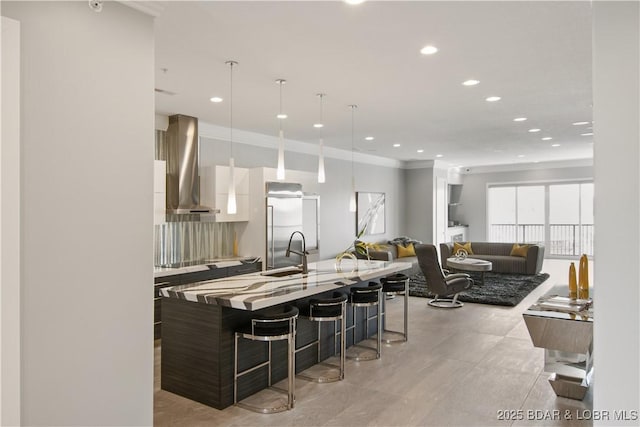 kitchen with a kitchen bar, modern cabinets, a sink, built in fridge, and wall chimney exhaust hood