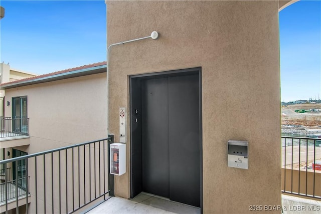 doorway to property featuring a balcony, elevator, and stucco siding