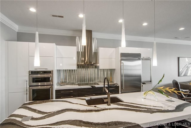 kitchen with a sink, appliances with stainless steel finishes, white cabinetry, wall chimney range hood, and modern cabinets