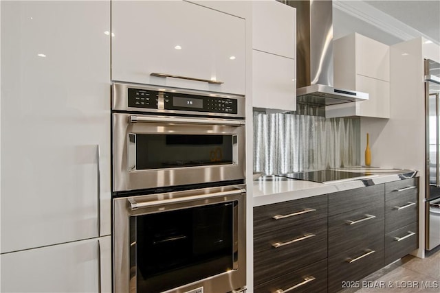 kitchen featuring wall chimney range hood, modern cabinets, white cabinets, and stainless steel double oven