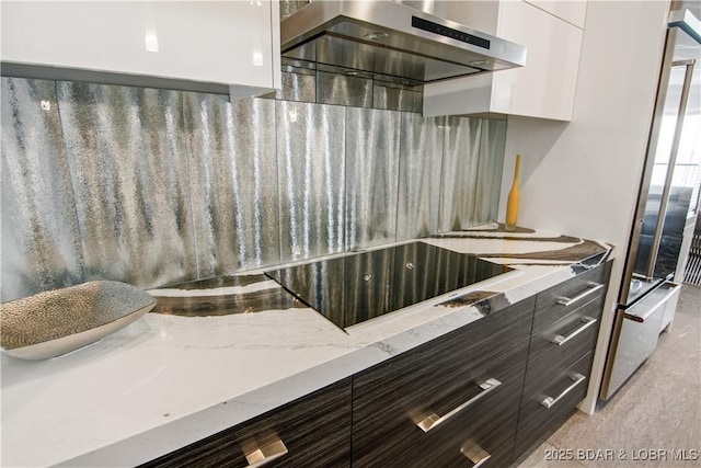 kitchen with black electric stovetop, light stone countertops, modern cabinets, and wall chimney exhaust hood